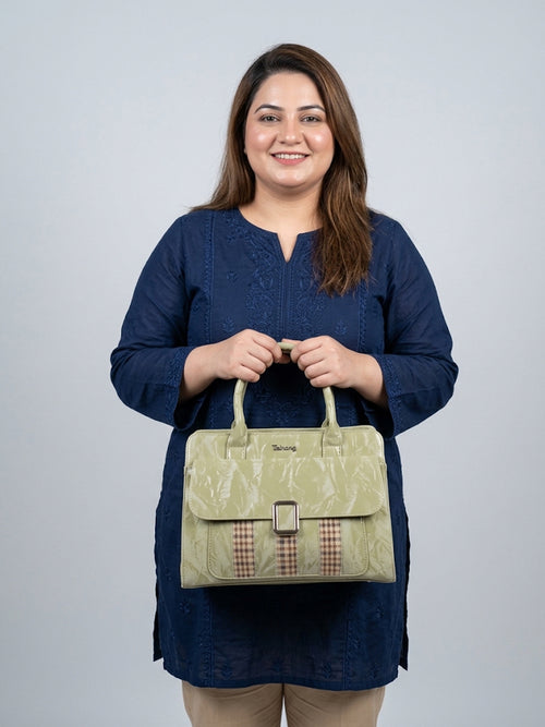 A woman wearing a navy blue tunic holds a light olive green textured handbag with a brown and beige gingham patterned accent strip on the front. The brand name 'Savvy' is visible on the bag against a solid light gray background.